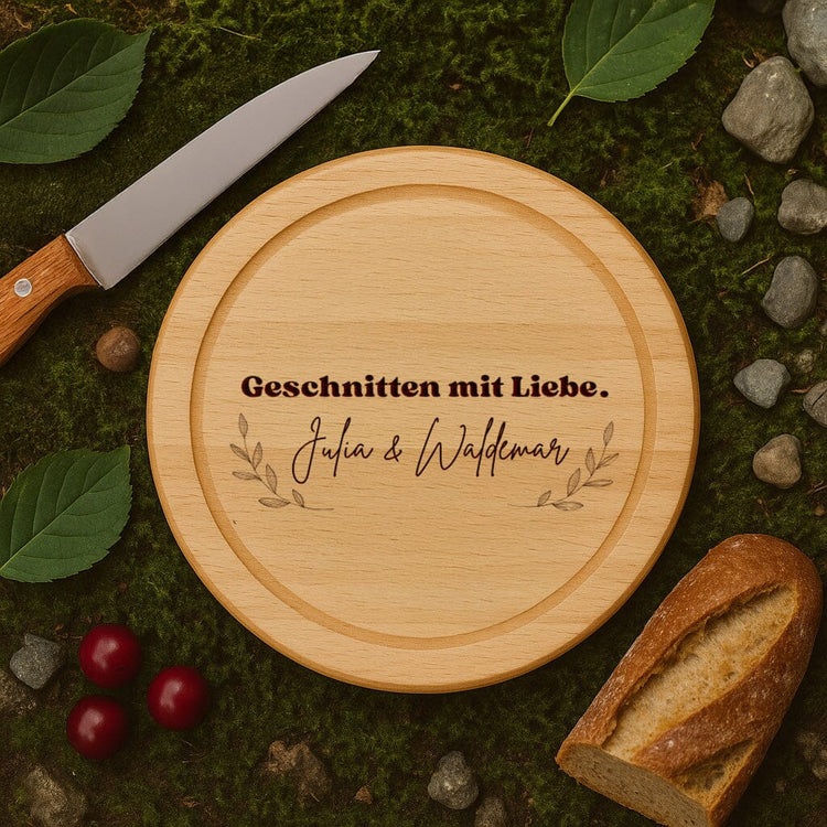Rundes Schneidebrett aus Buchenholz mit personalisierter Gravur und Namen auf natuerlichem Moos-Hintergrund.