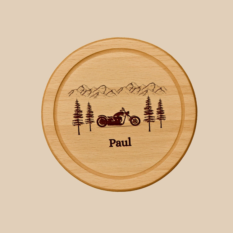 Rundes Holzbrett aus Buche mit personalisierter Gravur eines Motorrads, Berglandschaft und dem Namen Paul.