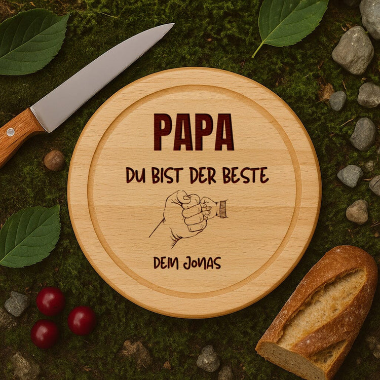 Rundes Schneidebrett aus Buche mit personalisierter Gravur "Papa du bist der Beste" und Faust-Motiv als Vatertagsgeschenk.