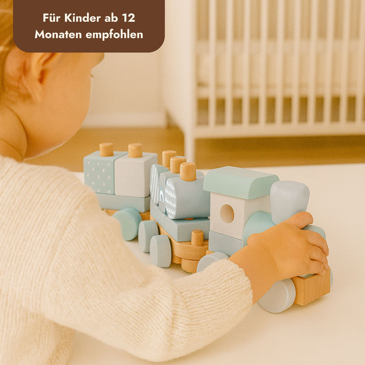 Kleinkind spielt mit pastellfarbenem Holz-Stapelzug aus Bauklötzen in Mint und Naturholz.