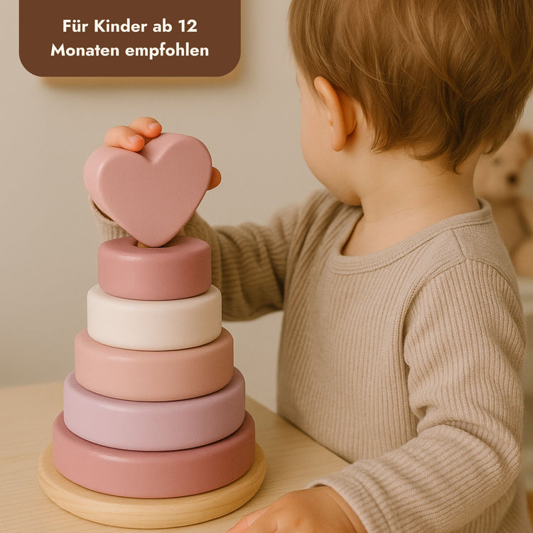 Kleinkind spielt mit pastellfarbenem Holz-Stapelturm mit Herzform-Topper in Rosa und Weiss.