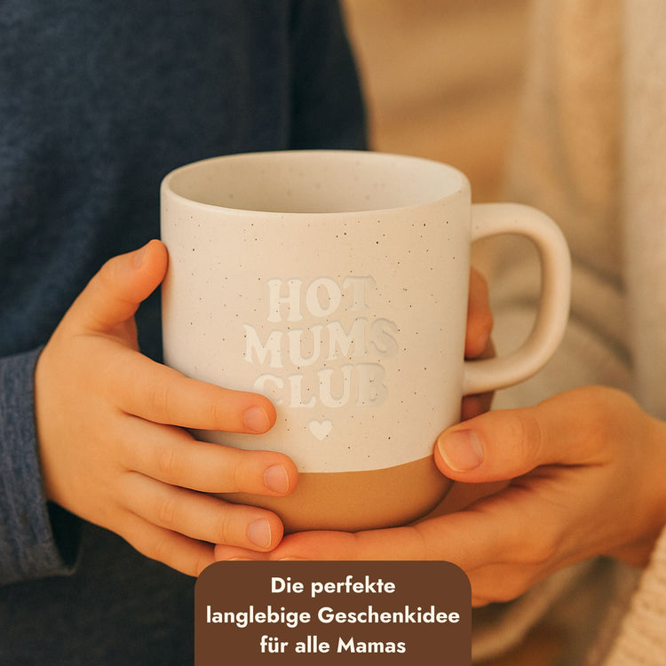 Beige Keramiktasse mit Hot Mums Club Schriftzug und Herz, gehalten von Mutter- und Kinderhänden als Muttertagsgeschenk.