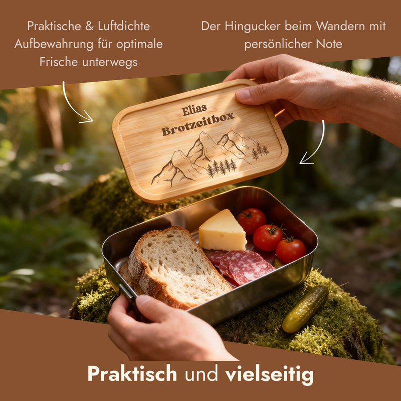 Personalisierte Edelstahl-Brotdose mit Bambusdeckel und Bergmotiv-Gravur, gefuellt mit Brotzeit in der Natur.