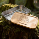 Personalisierte Edelstahl-Brotdose mit Bambusdeckel, Campervan-Gravur und Name auf moosigem Baumstumpf im Wald.