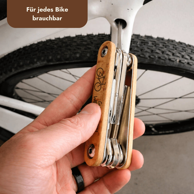 Fahrrad Multitool 9in1 aus Edelstahl mit personalisierter Gravur auf Holzgriff, gehalten vor einem Fahrradreifen.