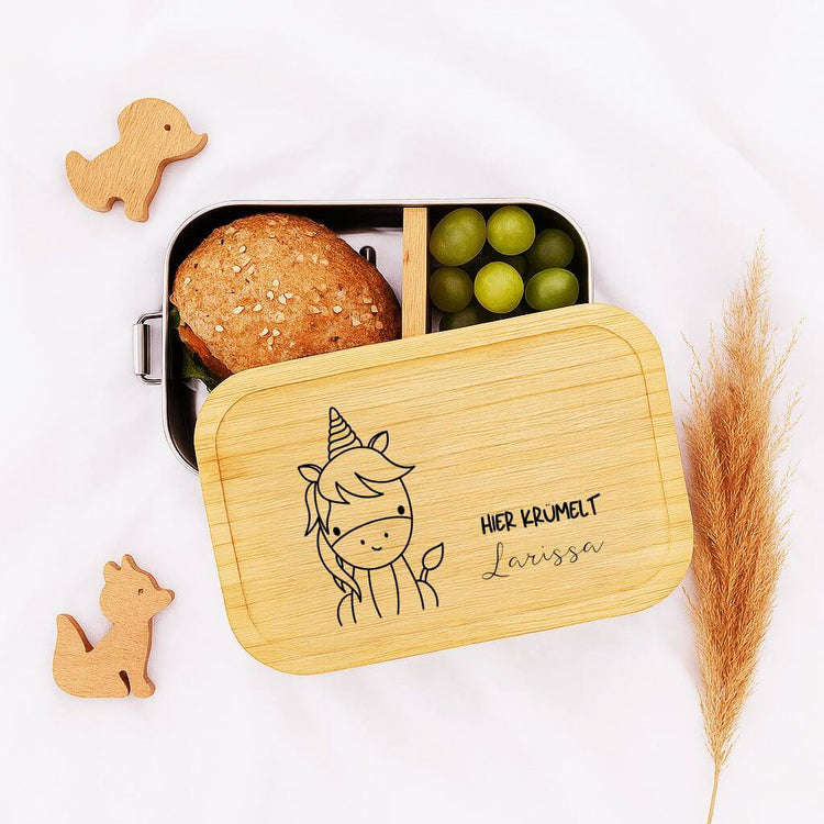 Personalisierte Edelstahl-Brotdose mit Bambusdeckel, Einhorn-Gravur und Name Larissa, gefuellt mit Broetchen und Trauben.