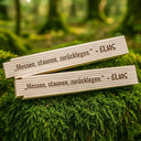 Personalisierter Zollstock aus Holz mit Namensgravur und Spruch auf moosigem Waldboden liegend.