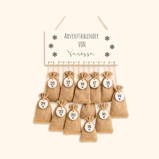 Personalisierter Adventskalender mit Jutesaeckchen und Namensschild vor cremefarbenem Hintergrund.