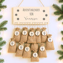 Personalisierter Adventskalender aus Holz mit Namensgravur und nummerierten Jutesaeckchen mit Schneeflocken-Motiv.