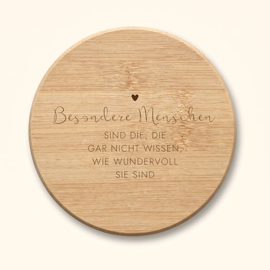 Runder Bambus-Untersetzer mit graviertem Herz und Spruch „Besondere Menschen sind die, die gar nicht wissen, wie wundervoll sie sind“ vor cremefarbenem Hintergrund.