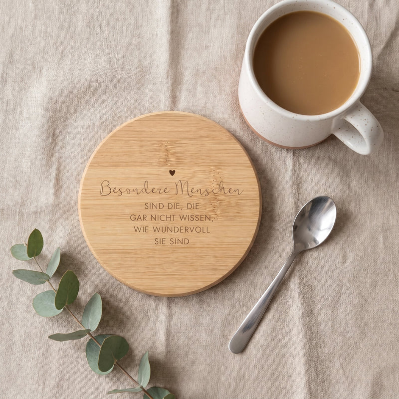Gravierter Bambus-Untersetzer von oben auf Leinen neben einer Tasse Kaffee, Eukalyptus und Löffel.