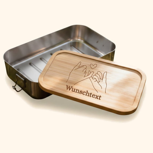 Edelstahl-Brotdose mit graviertem Bambusdeckel und personalisiertem Wunschtext auf moosigem Baumstumpf im Wald. — vor cremefarbenem Hintergrund.