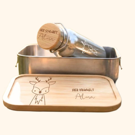 Kinder Brotdose und Trinkflasche aus Edelstahl mit Gravur vor cremefarbenem Hintergrund.