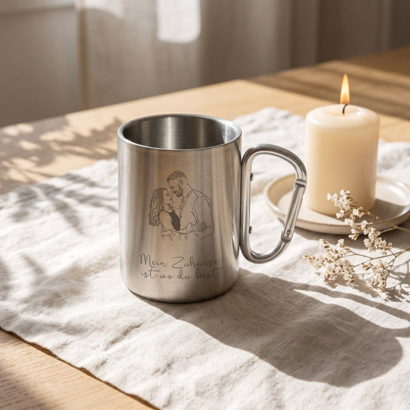 Campingbecher Silber mit Gravur auf Leinen neben einer Kerze und Trockenblumen.