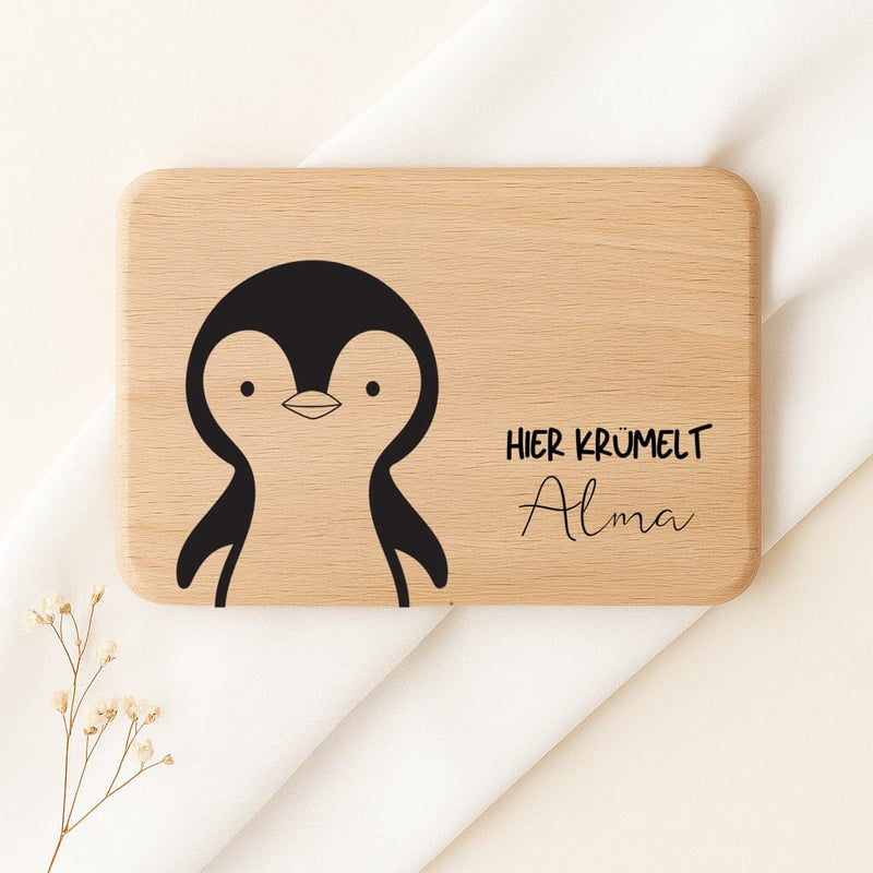 Personalisiertes Frühstücksbrettchen aus Buche mit Pinguin-Motiv und Gravur Hier krümelt Alma.