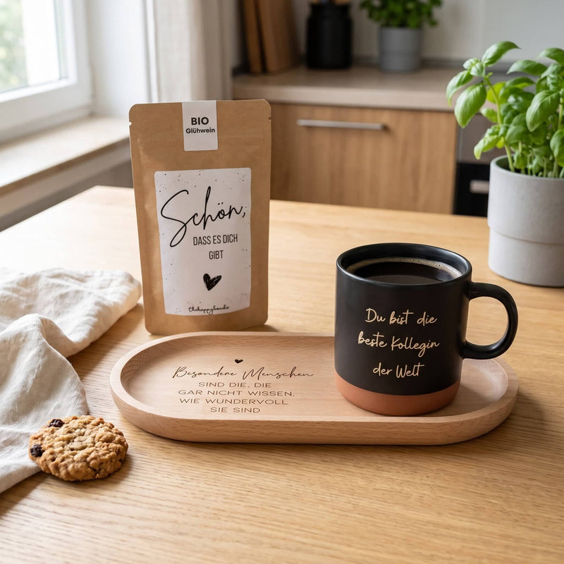 Personalisierte Tasse auf graviertem Holz-Tablett neben dem Sprüche-Tütchen auf einem hellen Küchentisch im Tageslicht.
