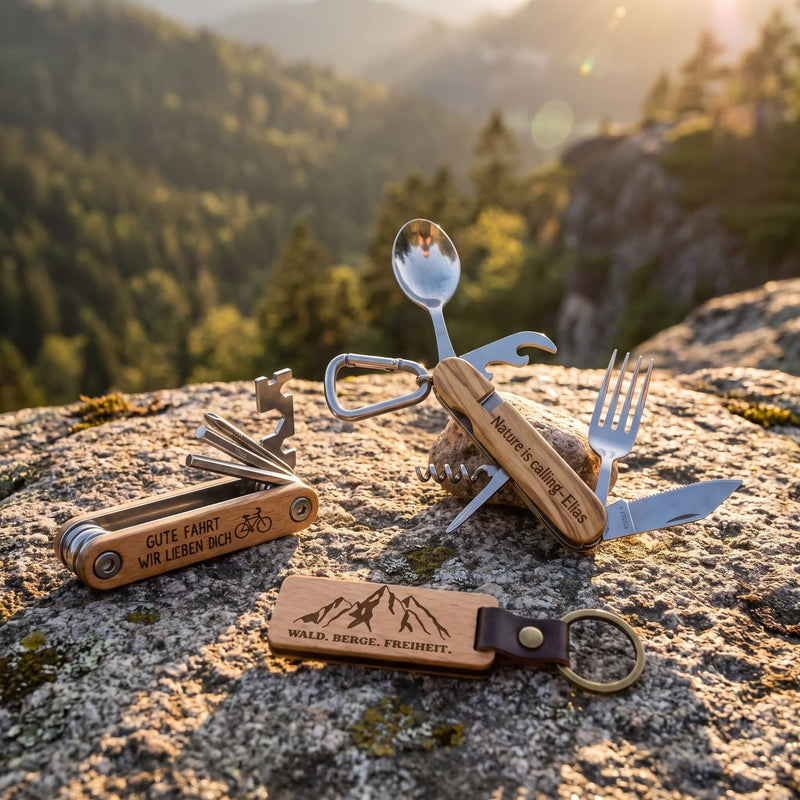 3er Set Outdoor auf einem Felsen am Aussichtspunkt: Campingbesteck, Fahrrad-Multitool und Holz-Schlüsselanhänger mit Bergmotiv.