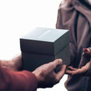 Elegante schwarze Happy Box Geschenkbox wird liebevoll von Hand zu Hand ueberreicht.