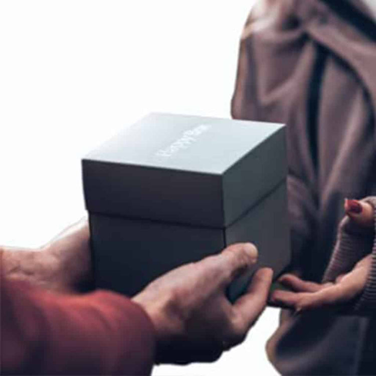 Elegante schwarze Happy Box Geschenkbox wird liebevoll von Hand zu Hand ueberreicht.