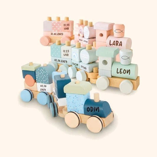 Personalisierte Holz-Stapelzuege mit gravierten Namen und Geburtsdaten in Pastell-Rosa, Mint und Blau. — vor cremefarbenem Hintergrund.