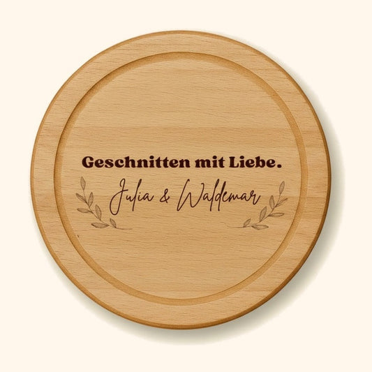 holzbrett personalisiert buche rund 25cm geschnitten mit liebe vor cremefarbenem Hintergrund.