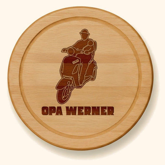 Rundes Schneidebrett aus Buche mit personalisierter Gravur eines Motorradfahrers und dem Namen Opa Werner. — vor cremefarbenem Hintergrund.