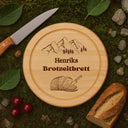 Rundes Brotzeitbrett aus Buchenholz mit personalisierter Gravur, Bergmotiv und Name auf natuerlichem Mooshintergrund.