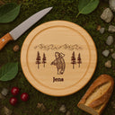 Rundes Schneidebrett aus Buche mit personalisierter Holzfäller-Gravur, Name Jens, Berglandschaft und Tannen.