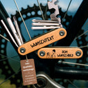 Personalisierbares Fahrrad Multitool 9in1 aus Edelstahl mit Holzgriff und individueller Lasergravur vor Fahrradkette.