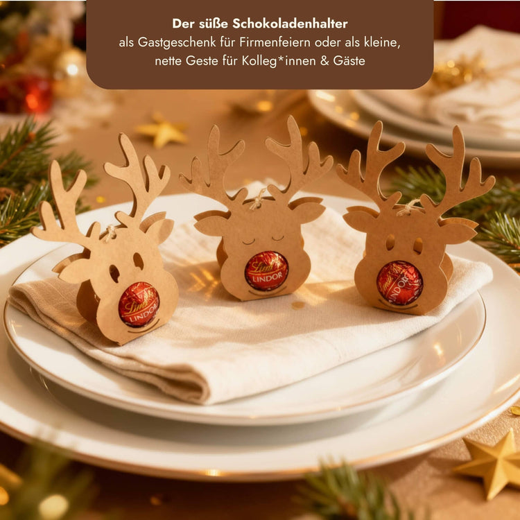 Drei Rentier-Schokoladenhalter aus Holz mit Lindt Lindor Kugeln auf weihnachtlich gedecktem Teller als Gastgeschenk.