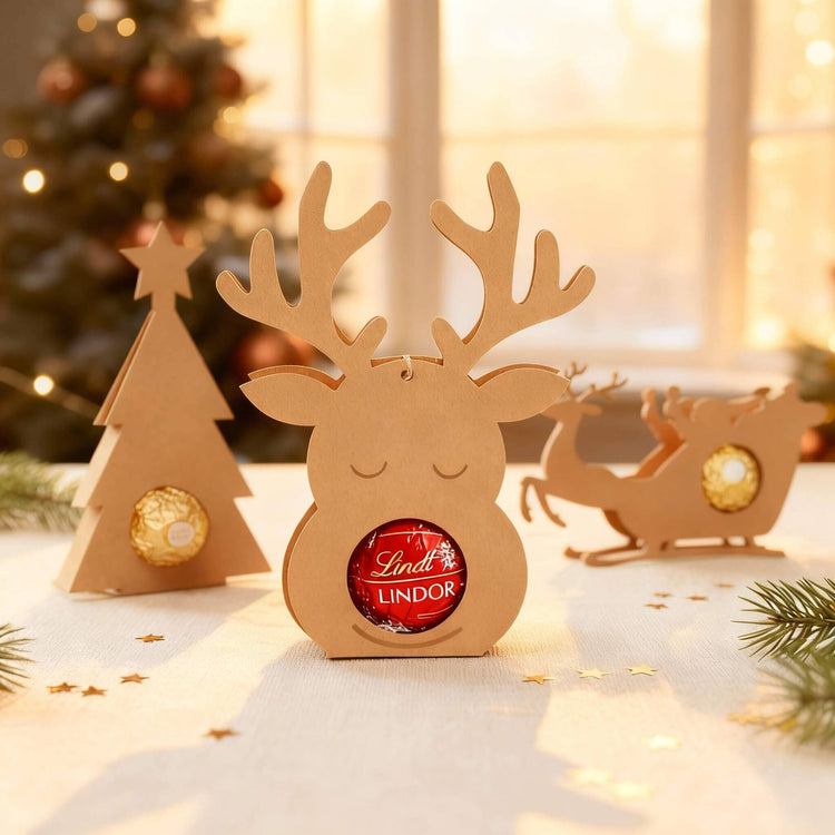 Rentier-Schokoladenhalter aus Holz mit Lindt Lindor Kugel in weihnachtlicher Dekoration mit Tannenbaum und Schlitten.