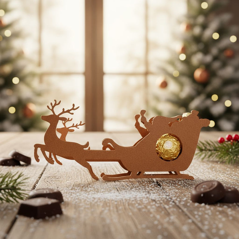 Rentier-Schlitten Schokoladenhalter aus Holz mit goldener Praline vor weihnachtlicher Dekoration.