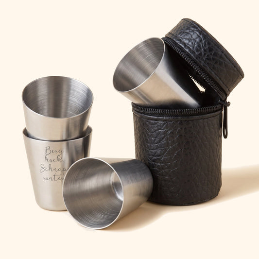Schnapsgläser-Set aus Edelstahl: vier Becher und schwarzes Etui, vorderer Becher mit Beispielgravur „Berg hoch. Schnaps runter.“, Packshot.