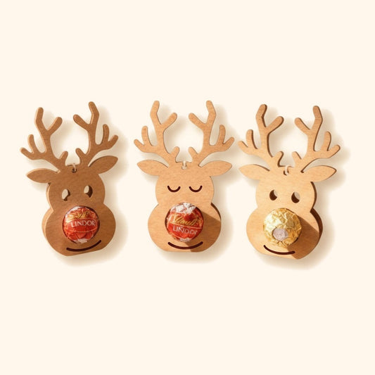 Drei Rentier-Schokoladenhalter aus Holz mit Lindor-Kugeln als weihnachtliche Geschenkidee. — vor cremefarbenem Hintergrund.