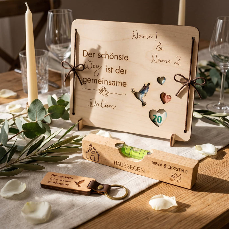 Geldgeschenk-Box mit Gravur, Haussegen Wasserwaage und Schlüsselanhänger auf einem festlich gedeckten Hochzeitstisch mit Eukalyptus und Kerzen.