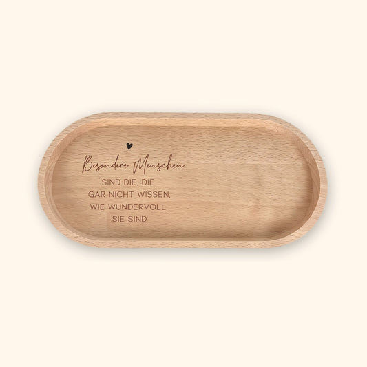 Ovales Holz-Tablett aus Buche mit gravierten Herz und Spruch „Besondere Menschen sind die, die gar nicht wissen, wie wundervoll sie sind“ vor cremefarbenem Hintergrund.