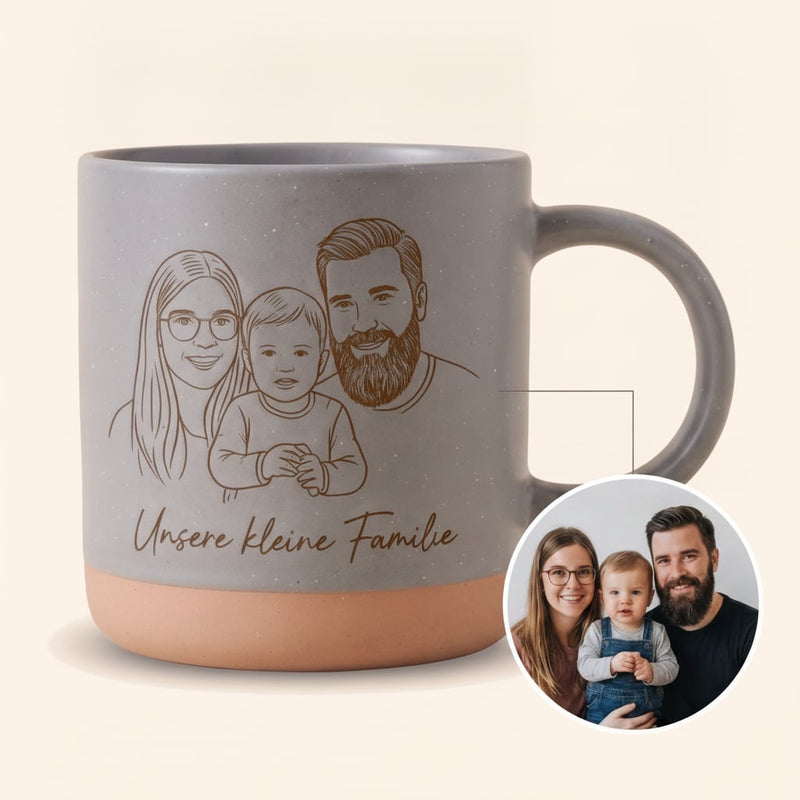 Graue Keramik Tasse mit dunkler gravierter Familien-Illustration und Schriftzug Unsere kleine Familie — vor cremefarbenem Hintergrund.