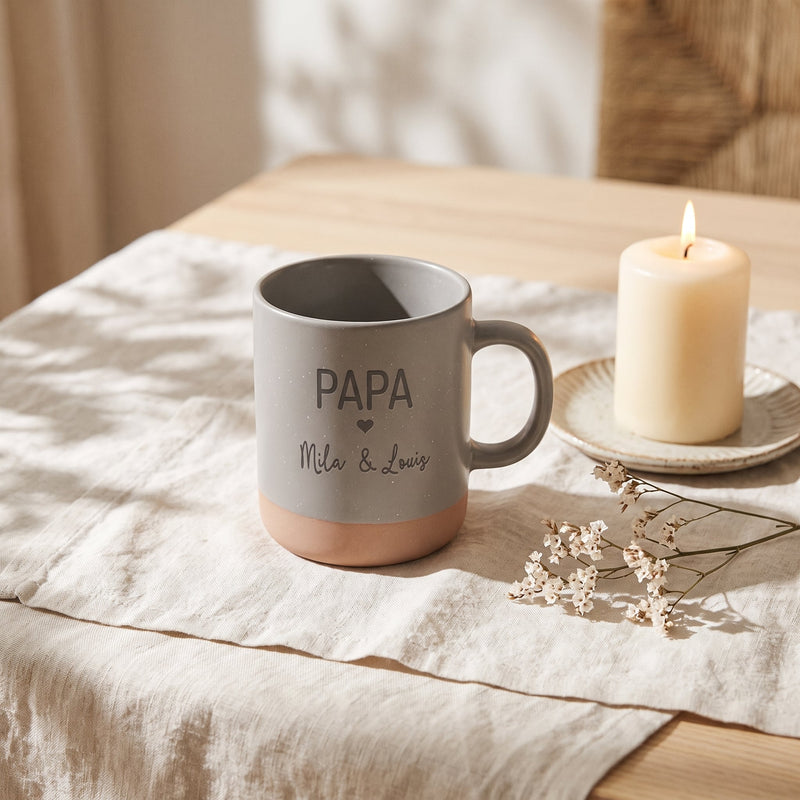 Tasse Papa personalisiert mit Kindernamen und Herz in grau: papa, auf Leinen mit Kerze und Trockenblumen.