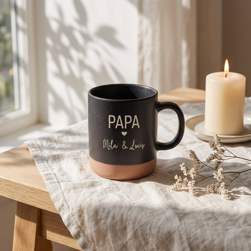 Tasse Papa personalisiert mit Kindernamen und Herz in schwarz: papa, auf Leinen mit Kerze und Trockenblumen.