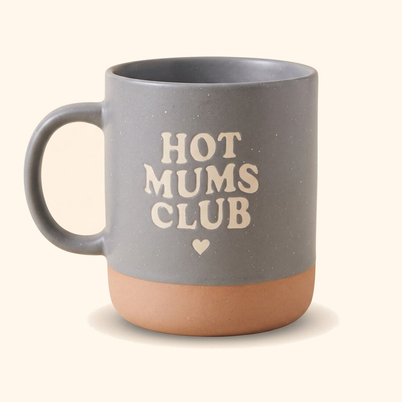 Graue Keramiktasse Pascal mit Aufdruck Hot Mums Club, als Geschenk für Mamas in der Hand gehalten. — vor cremefarbenem Hintergrund.