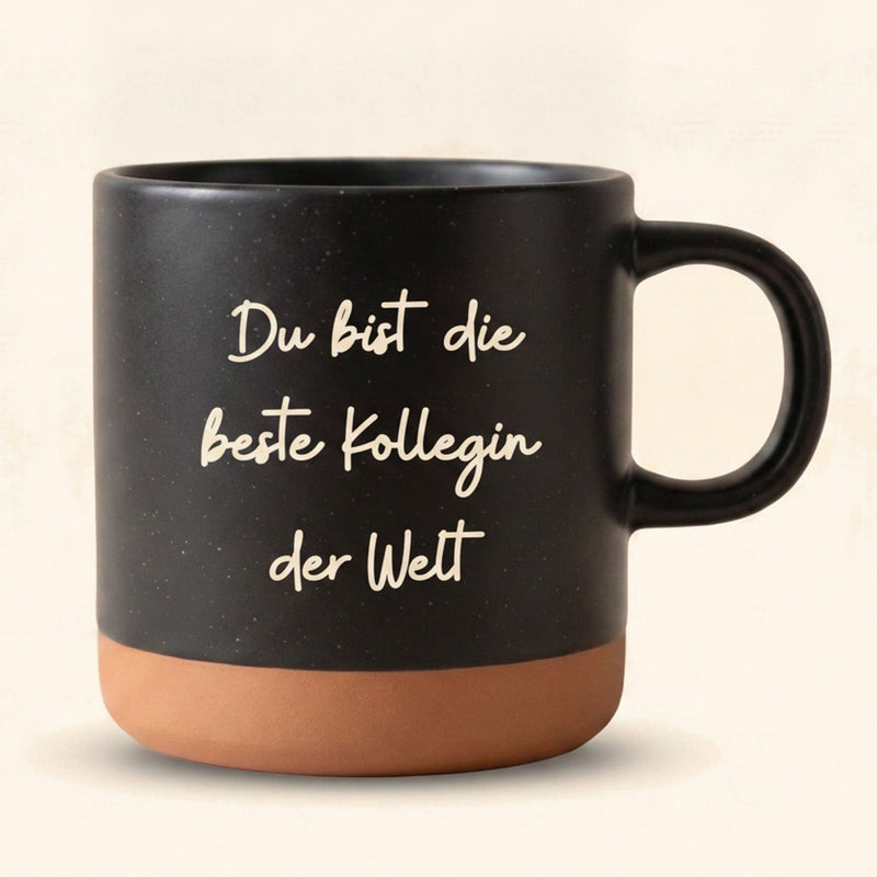 Schwarze Keramik Tasse mit gravierter Handschrift Du bist die beste Kollegin der Welt — vor cremefarbenem Hintergrund.