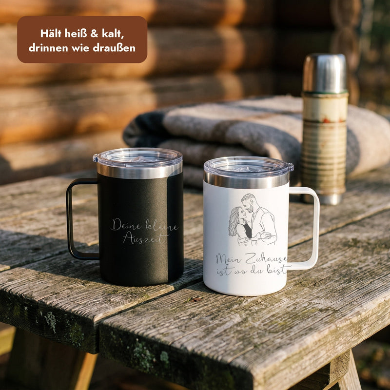 Gravierter schwarzer und weißer Thermobecher auf einem Holztisch vor einer Hütte, Text: Hält heiß und kalt, drinnen wie draußen.