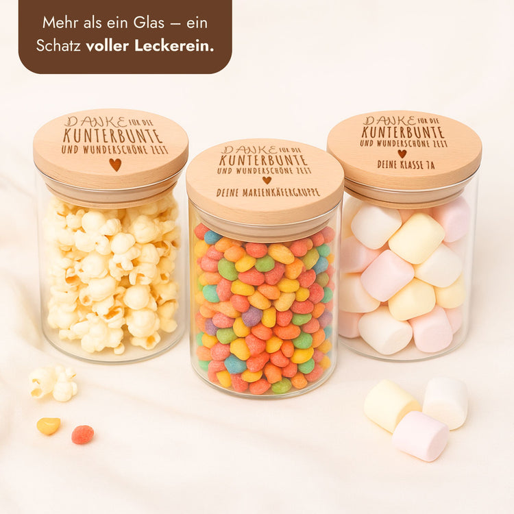 Drei Vorratsgläser mit graviertem Holzdeckel und Danke-Schriftzug, gefüllt mit Popcorn, bunten Bonbons und Marshmallows.