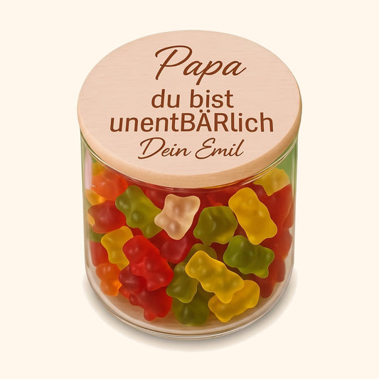 Vorratsglas mit graviertem Holzdeckel und Aufschrift Papa du bist unentBÄRlich, gefuellt mit bunten Gummibaerchen. — vor cremefarbenem Hintergrund.