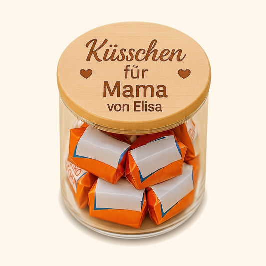 Vorratsglas mit graviertem Holzdeckel gefuellt mit Schokoladenkuesschen als personalisiertes Geschenk fuer Mama. — vor cremefarbenem Hintergrund.