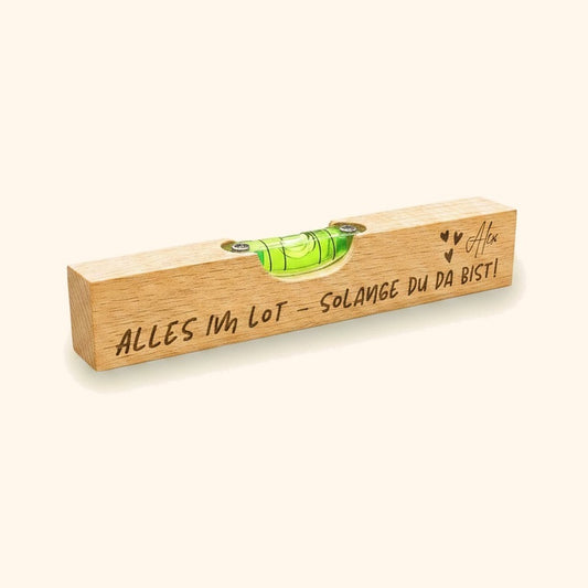 Personalisierte Wasserwaage aus Buche mit Gravur Alles im Lot vor cremefarbenem Hintergrund.