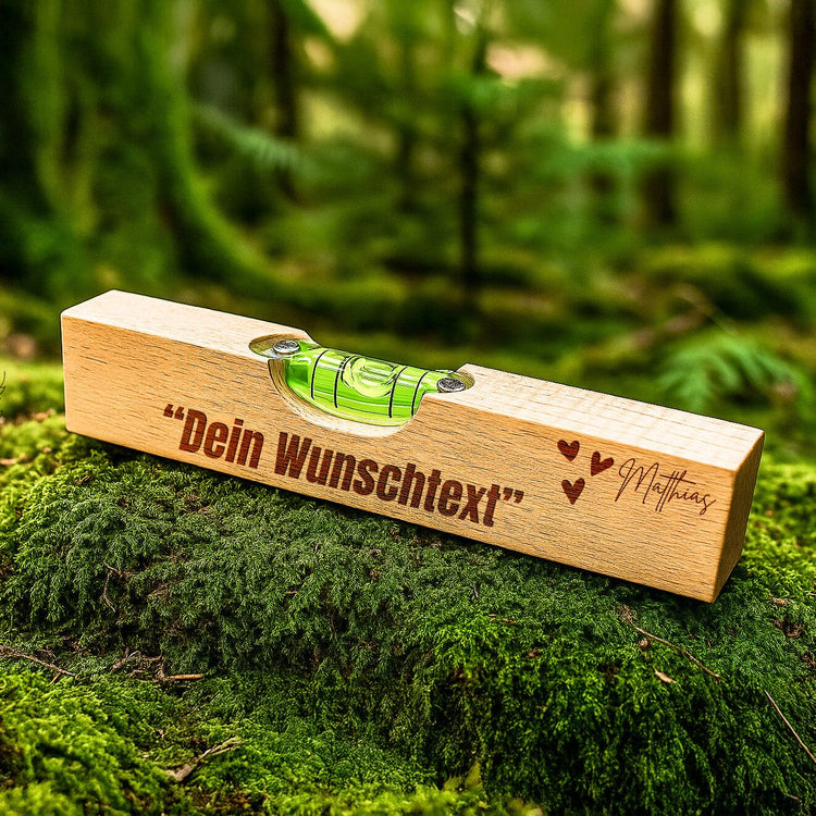 Personalisierte Wasserwaage aus Buchenholz mit individueller Gravur und Wunschtext auf moosigem Waldboden.