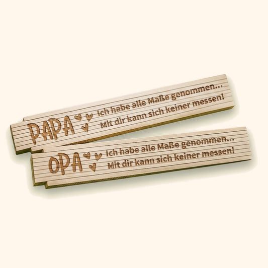Personalisierte ADGA-Zollstöcke aus Holz mit Gravur für Papa und Opa auf moosigem Waldboden. — vor cremefarbenem Hintergrund.